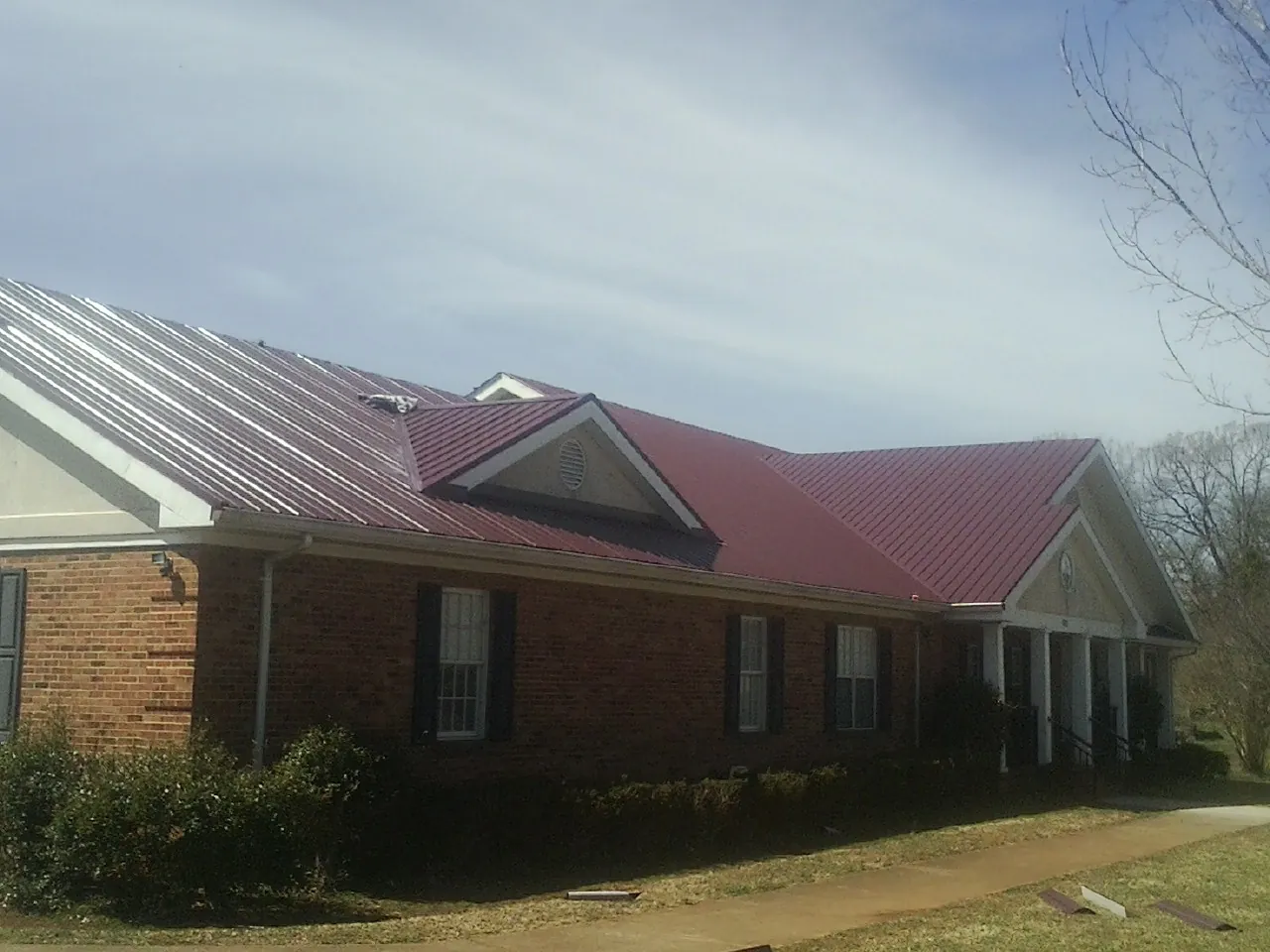 Red metal roof with gabled entries on a long brick building, from a Hail Damage Roof Repair job in Toms River