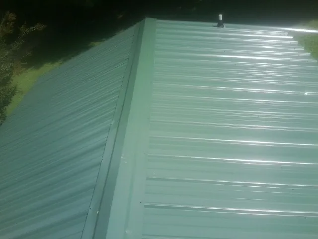 New green metal panels meeting at the ridge of a roof — Flat Roof Repair work by our crew in Toms River
