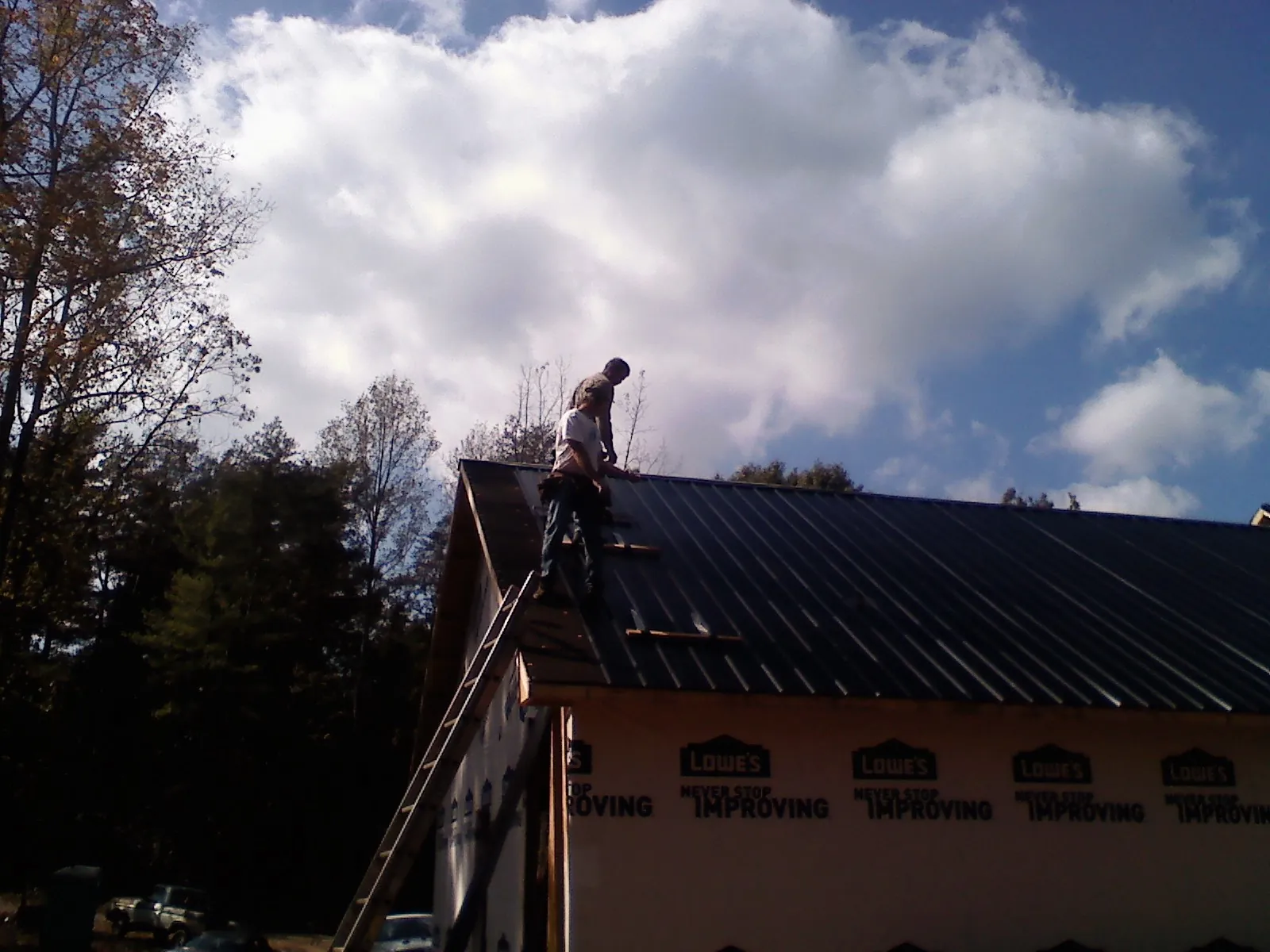 Roofer fastening dark metal panels high against a cloudy sky, from a Roof Inspection job in Toms River