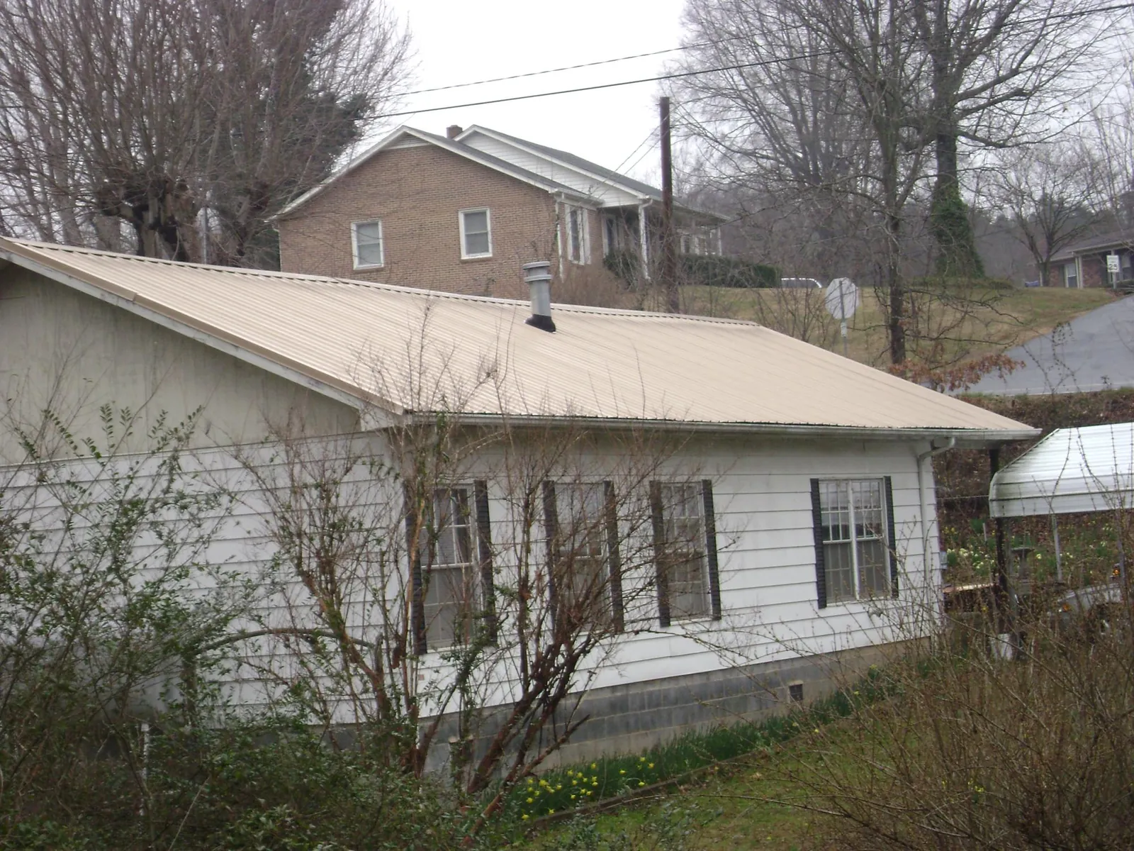 Tan metal roof on a white sided house set into a hillside — Commercial Roofing by Roofing Brothers in Toms River